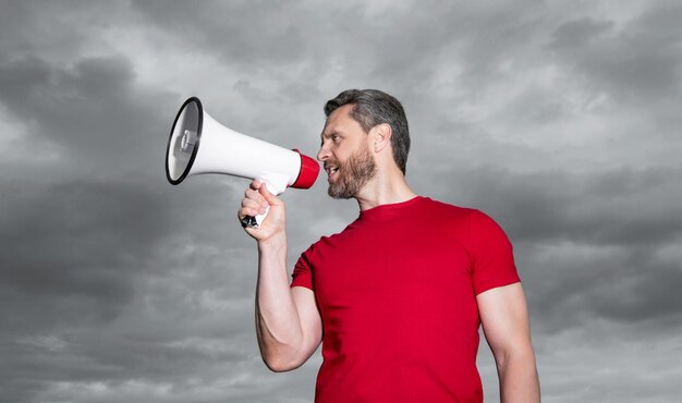 Man in red shirt announcing in loudspeaker on sky background