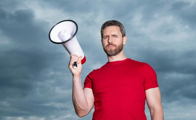 Man in red shirt hold loudspeaker on sky background