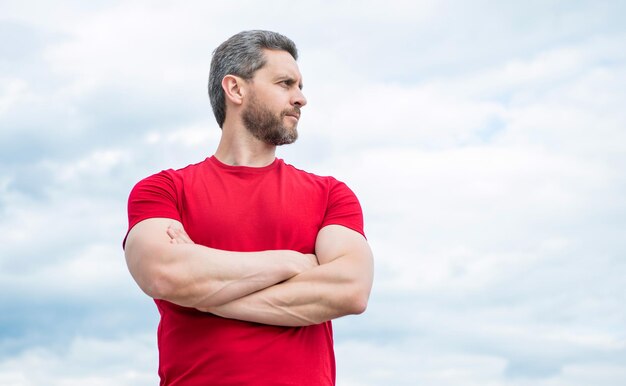 Man in red shirt outdoor on sky background crossed hands