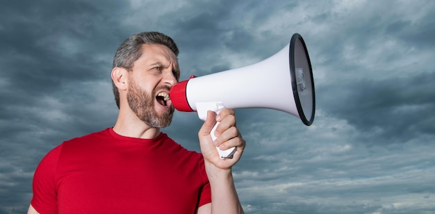 Man in red shirt screaming in loudspeaker on sky background