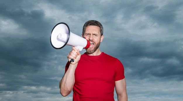 Man in red shirt shout loud in loudspeaker on sky background