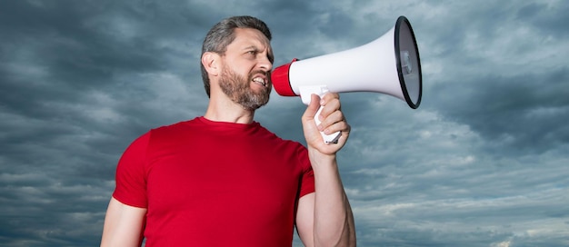 Man in red shirt shout in loudspeaker on sky background\
advertisement