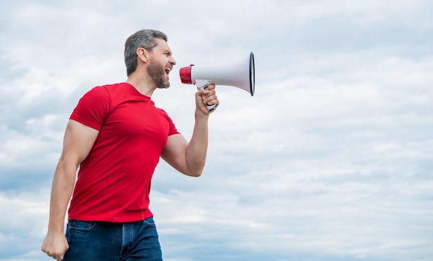 man in red shirt shouting in loudspeaker on sky background