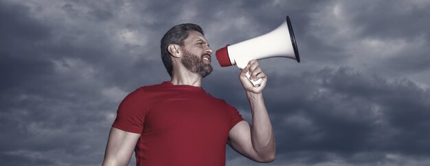 Man in red shirt speaking in loudspeaker on sky background