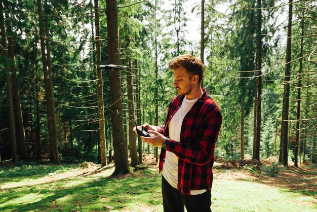 Man in a red shirt with a remote control in his hands flies on a drone in the woods