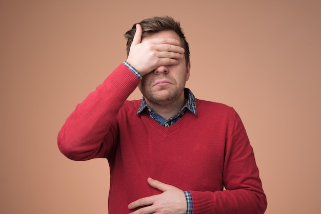 Man in red sweater covering eyes trying to stay away from problems