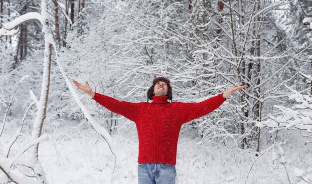 빨간 스웨터를 입은 한 남자가 눈 덮인 숲에 손을 들고 서있다. 가족 겨울 방학.