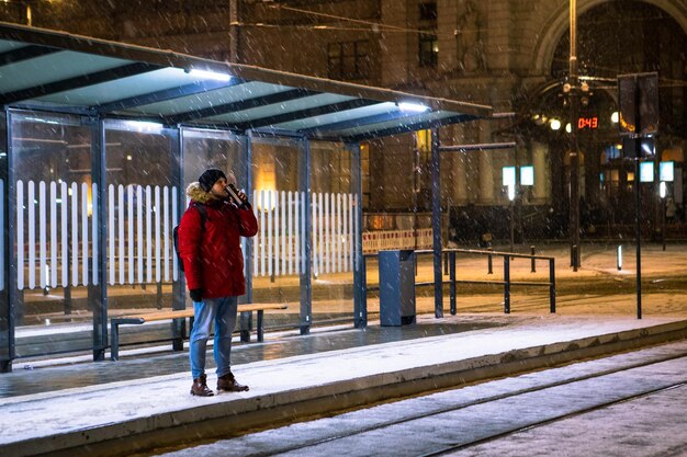 Man in red winter coat standing at bus tram stop waiting for public transport