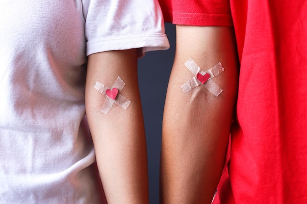 Man in red and woman in white Tshirt with hands taped patch after giving blood with red heart Bloo