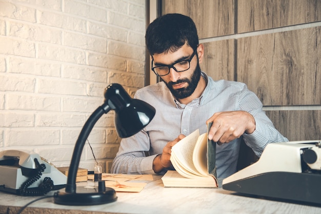 Man reding book and typewriter on desk