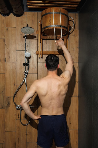 Man refreshing himself anfter hot sauna with cold water from wooden bucket