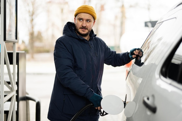 Uomo che rifornisce di carburante la sua auto suv americana alla stazione di servizio quando fa freddo