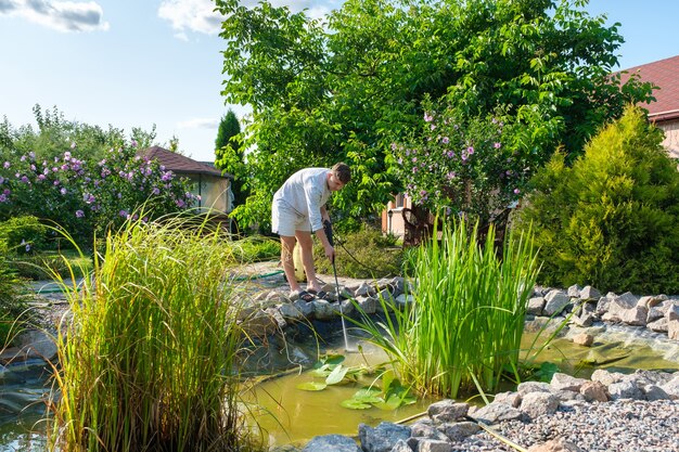 Man reinigt tuinvijverbodem met hogedrukreiniger van modder en slib