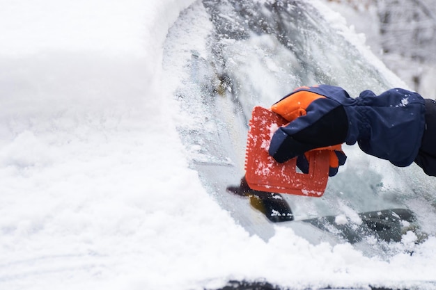 Man reinigt zijn auto na een sneeuwval Sneeuw van de voorruit verwijderen Ijs schrapen Winter autoruiten poetsen