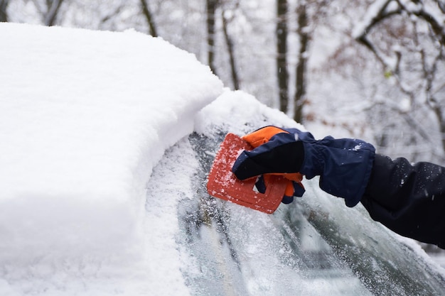 Foto man reinigt zijn auto na een sneeuwval sneeuw van de voorruit verwijderen ijs schrapen winter autoruiten poetsen