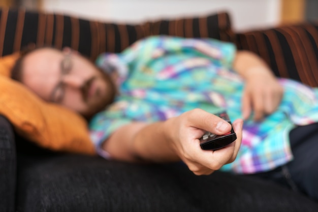 Man relaxing in sofa with remote control watching tv. 