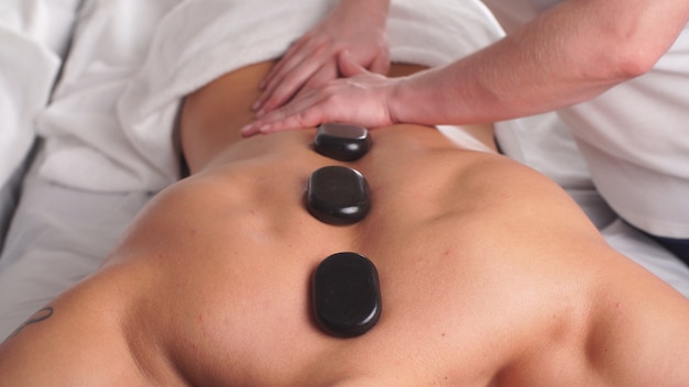 Man relaxing in wellness spa center with hot stones on body.