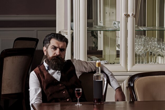 Man relaxing with wine in restaurant hipster with beard sitting at table with bottle and glass alcohol and appetizer