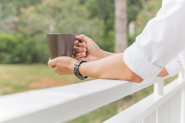 Foto man relaxjng hand met koffiemok terwijl je op balkon staat.