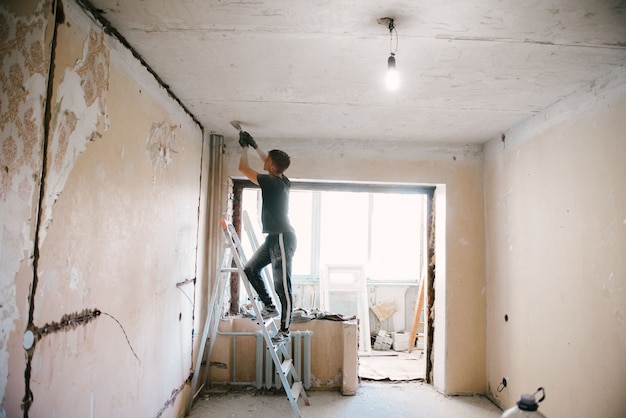 A man removes old paint from the ceiling with a spatula