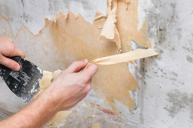 A man removes old wallpaper with a spatula and a spray bottle with water.