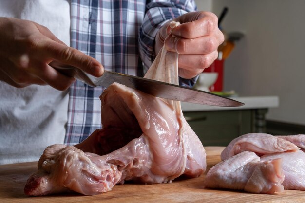 男は生の鶏の胸肉から皮を取り除きます 鶏肉をバラバラに切る