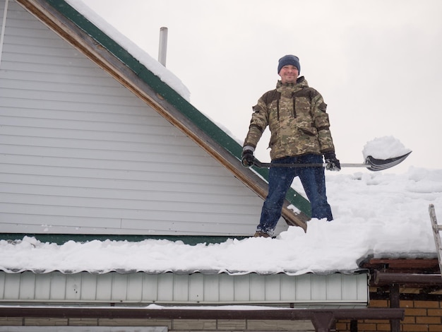 A man removes snow from the roof of a completely snowcovered\
house with a shovel a lot of fresh snow after a blizzard hard and\
dangerous work