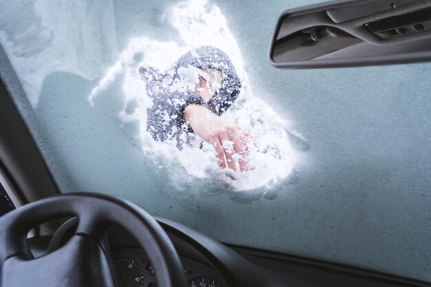 車のフロントガラスから雪を除去している男性