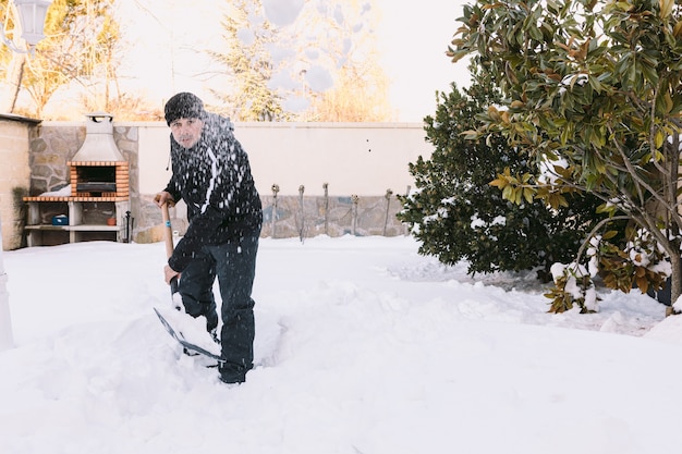 Человек убирает снег из сада своего дома с лопатой