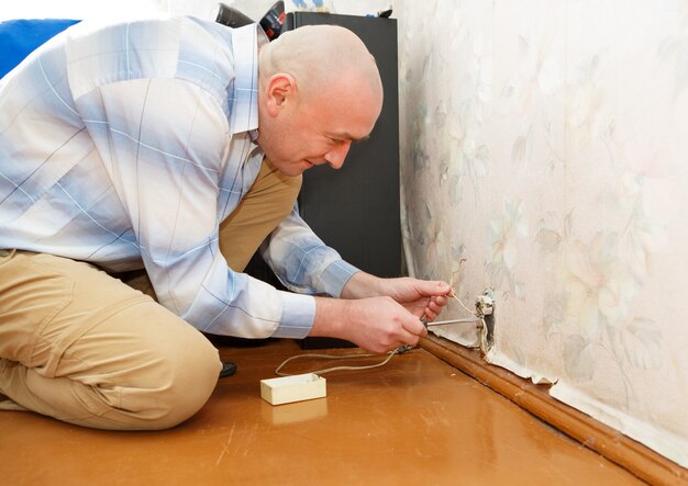 Man repairing an electrical outlet while sitting on the floor