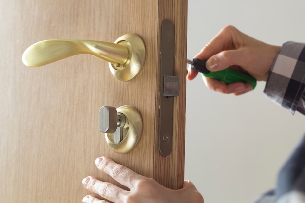 Photo the man repairs the locksmith, sets the door lock on the wooden door.