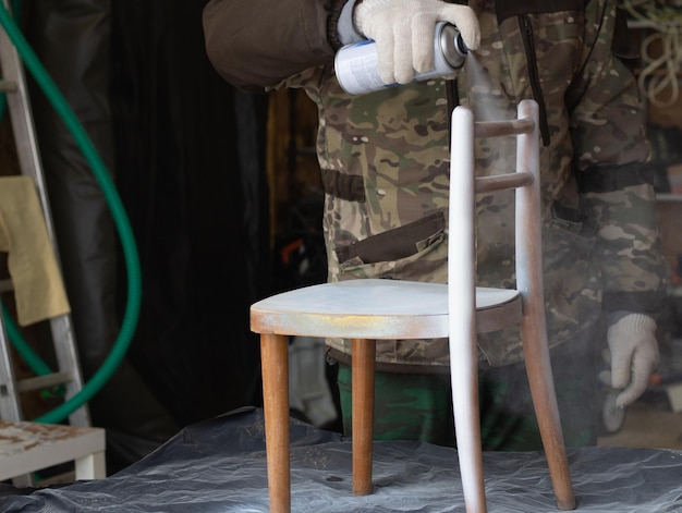 Мужчина ремонтирует старую мебель, красит детский стул аэрозольной краской, концепция ручной работы