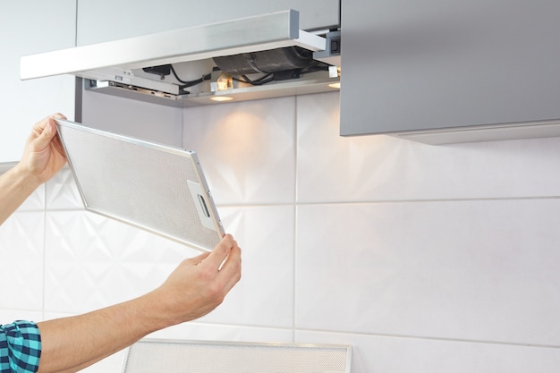 Man repairs range hood in the kitchen. Replacement filter in a cooker hood.