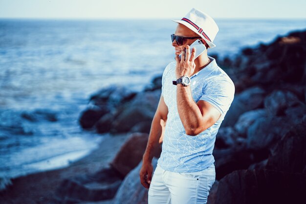 The man at the resort in a shirt blue and sunglasses, hat on the sea