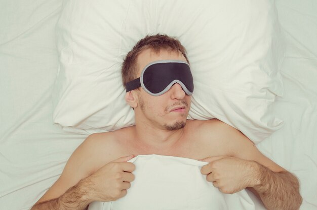 Man resting in a mask for sleep. Stubble on his face. Tired man