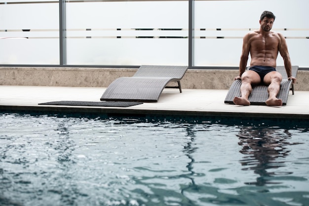 Man Resting On Sun Loungers By Swimming Pool