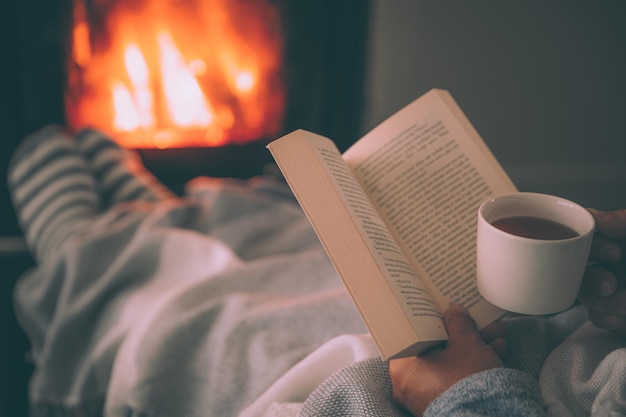 Man resting with hot drink cup and book near fireplace