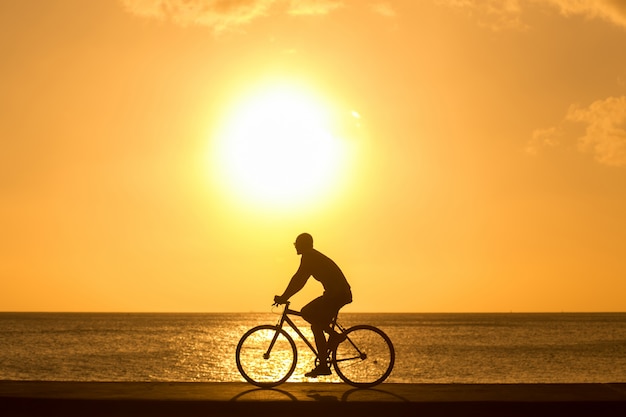 Man ride bicycles outdoors against sunset. Silhouette.