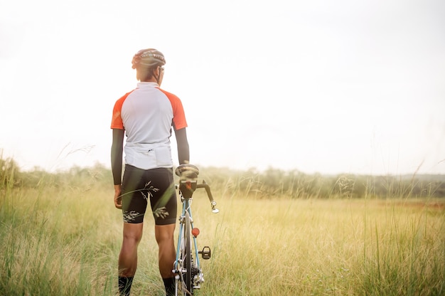 Photo a man ride on bike on the road. man riding vintage sports bike for evening exercise. a man ride bicycle to breathe in the fresh air in midst of nature, meadow, forest, with evening sun shining through