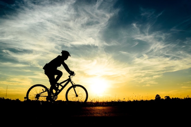 A man rides a bicycle on the road at sunset sky background.