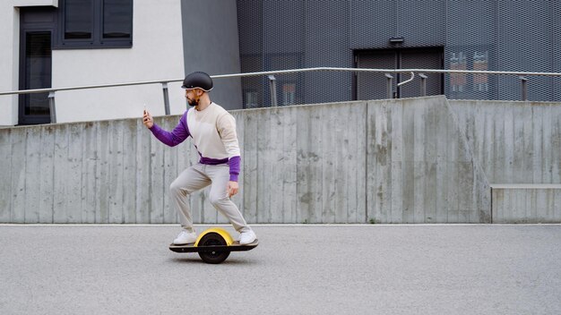 Man rides at electric skateboard and looks at smartphone Text space Copy Spcae Modern building in background High quality photo