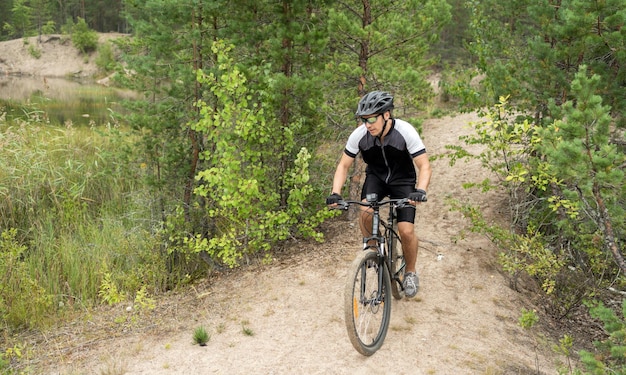 한 남자가 헬멧을 쓰고 녹색 숲의 길에서 장비를 타고 산악 자전거를 탄다