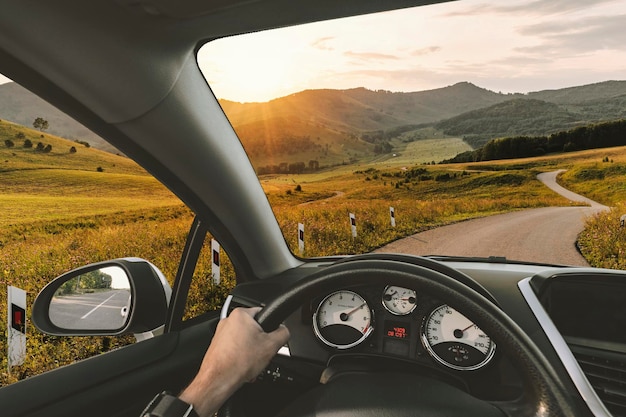 A man rides on a mountain road serpentine Beautiful road between the hills Summer landscape Driver's hands on a steering wheel of a car