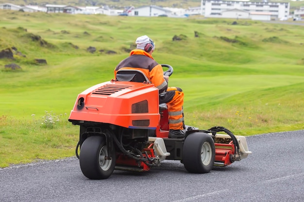 Man rides on a special machine to clean the grass of the Golf course Heimaey Island of the Vestmannaeyjar Archipelago Iceland