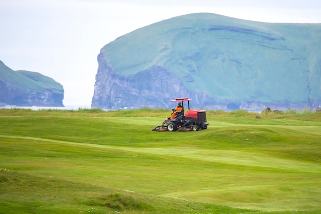 Man rides on a special machine to clean the grass of the Golf course Heimaey Island of the Vestmannaeyjar Archipelago Iceland