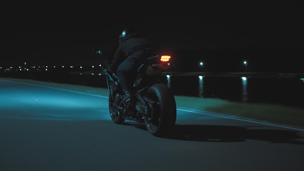 A man rides a sports motorcycle through the city at night against the backdrop of the river