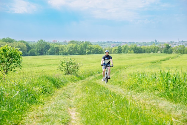 緑の大麦畑のコピースペースでトレイルで自転車に乗る男