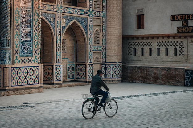 Foto uomo che guida una bicicletta vicino alla vecchia madrasa a bukhara