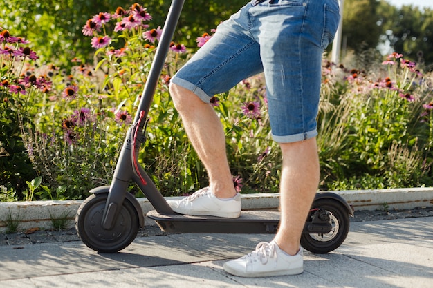 Photo man riding an ecofriendly electric kick scooter in a park in sunny weather on sidewalks. closeup