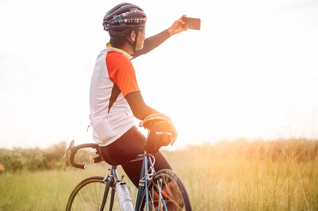 Photo a man riding vintage sports bike for evening exercise. a man ride bicycle to breathe in the fresh air in midst of nature, meadow, forest, with evening sun shining.  a man taking a selfie with bicycle.